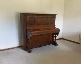 Upright piano being prepared for removal from a living room area.